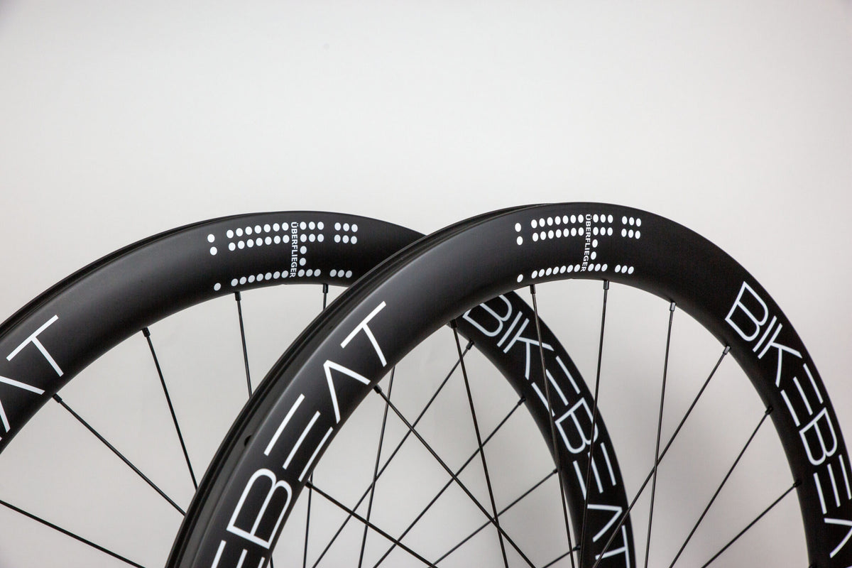 Two black carbon fiber Bike Beat Überflieger Pro 50 Disc wheels featuring white branding and dot-pattern decals.