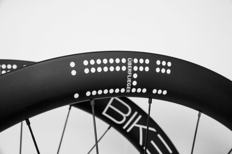 Black carbon fiber Bike Beat Überflieger Pro 50 Disc wheelset with white dotted patterns and the text ÜBERFLIEGER printed on the side.