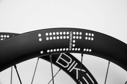 Black carbon fiber Bike Beat Überflieger Pro 50 Disc wheelset with white dotted patterns and the text ÜBERFLIEGER printed on the side.